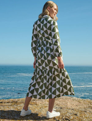 Model weas the Sunday Girl Matty Print Dress in green and white triangle print at the beach, standing with the ocean behind her.